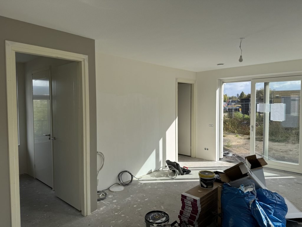 Nieuwbouwwoonkamer tijdens de afwerking, met gesausde wanden, verfemmers en dozen op de vloer