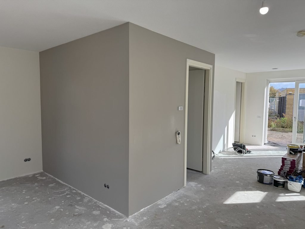 Nieuwbouwwoonkamer met een strak gesausde grijze wand en verfemmers op de betonvloer