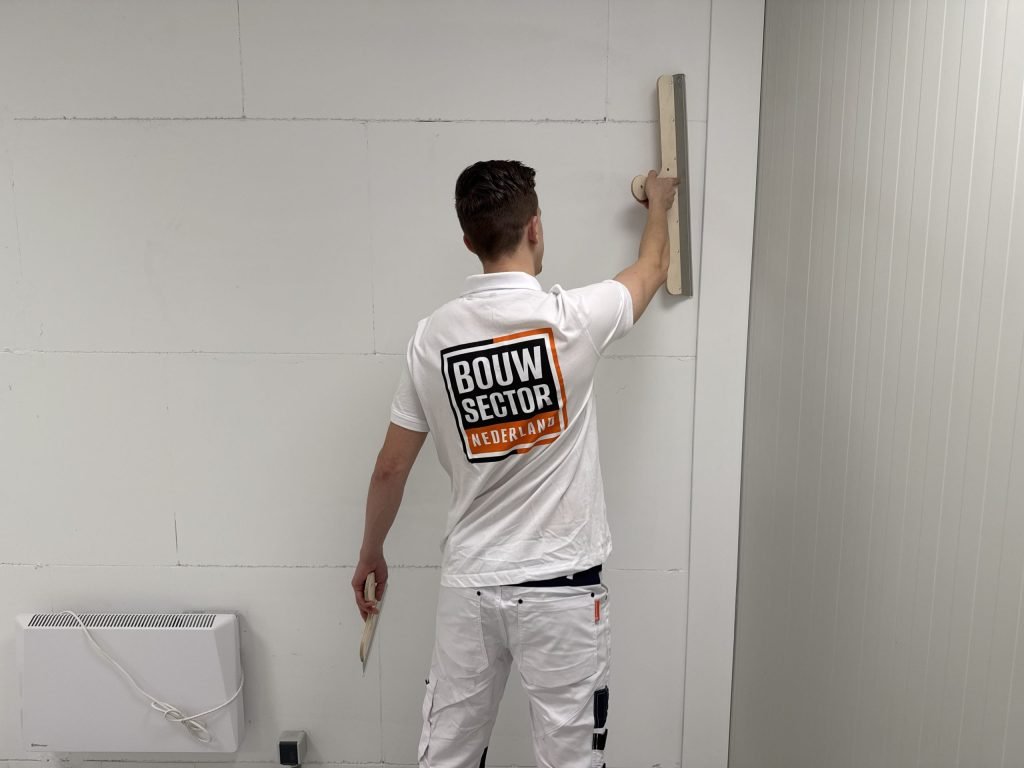 Stukadoor van Bouwsector Nederland zet een lange spaan tegen een wand met zichtbare plaatnaden