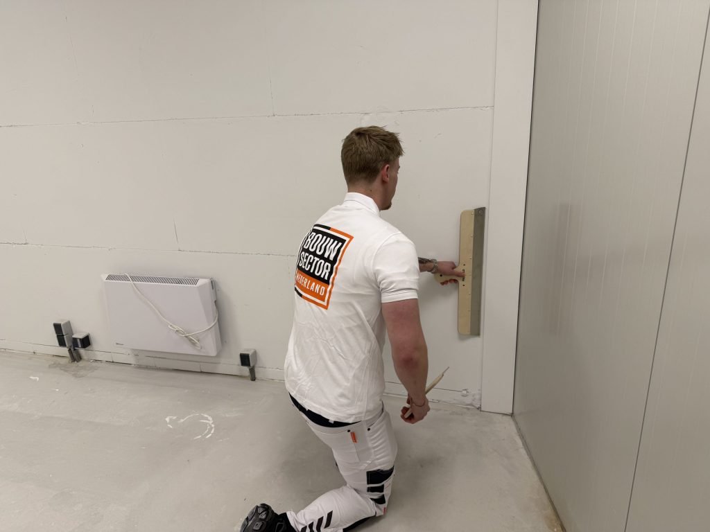 Stukadoor van Bouwsector Nederland werkt met een spaan onderaan een wand met zichtbare naden