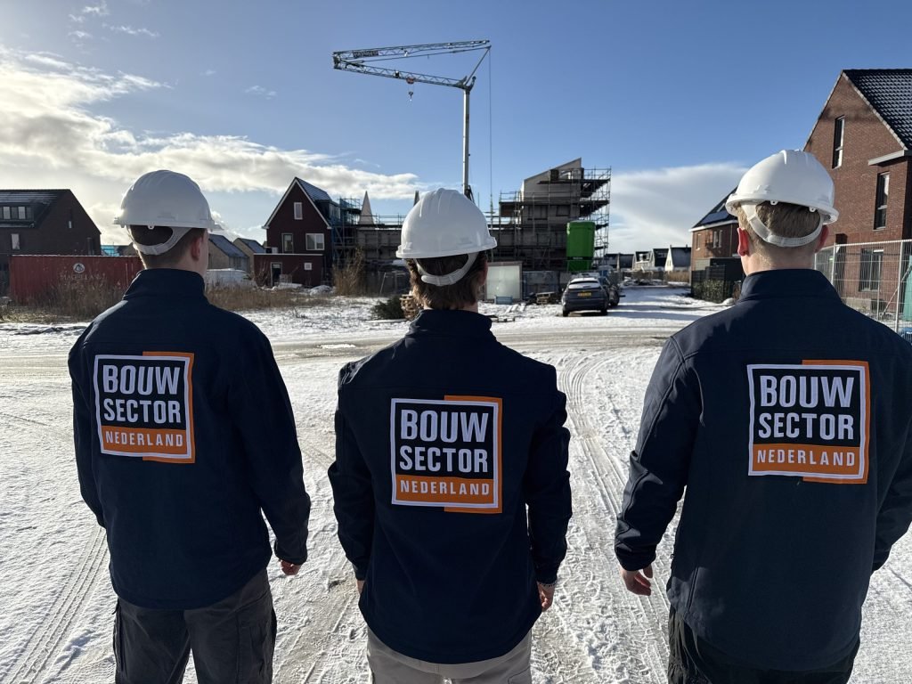 Drie vakmensen van Bouwsector Nederland met witte helm op een besneeuwde nieuwbouwstraat met een bouwkraan